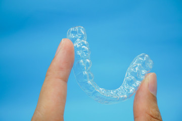 hand holding clear plastic retainer teeth that isolated on blue sky background. it's an equipment for orthodontist give the patient to orthodontic surgery in dental clinic or hospital - obrazy, fototapety, plakaty