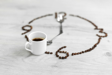 Coffee grains folded in the form of a clock on a wooden background. Instead of the number 7, a cup...