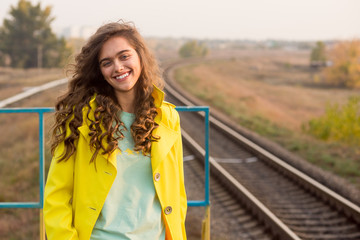 Smiling curly girl in a yellow coat in the fall. Portrait of a happy traveler girl. Student train ride