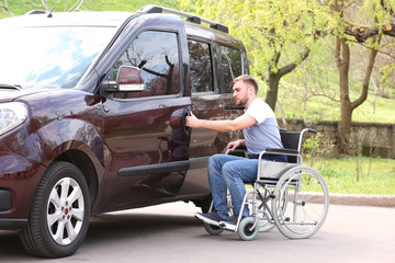 Young man in wheelchair opening door of his van outdoors