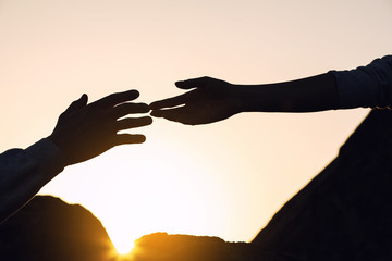 Silhouettes of man and woman helping each other to climb on hill against sunset, closeup