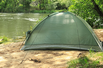 Modern camping tent on riverbank in wilderness