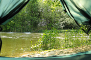 Calm river with forest on bank, view from camping tent