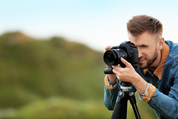 Male photographer taking picture of beautiful landscape with professional camera on green hill....