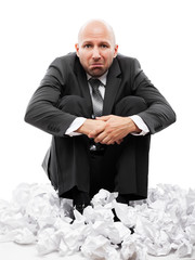 Businessman in depression sitting on crumpled torn paper document heap