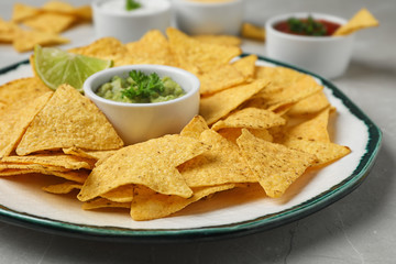 Plate of Mexican nacho chips with sauce on grey marble table, closeup