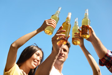 Young people holding bottles of beer against blue sky, focus on hands