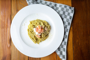 Spaghetti pasta with green pesto and cheese on wooden background