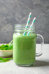 Mason jar of healthy green smoothie with fresh spinach on grey table