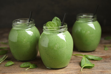 Jars of healthy green smoothie with fresh spinach on wooden table