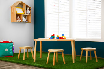 Stylish playroom interior with wooden table and stools