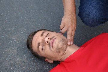 Passerby checking pulse of unconscious young man outdoors © New Africa