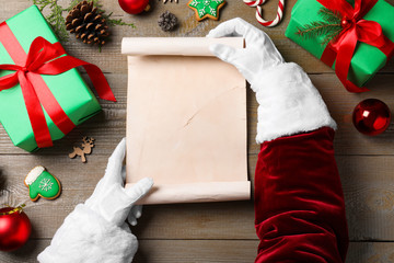 Santa Claus holding empty paper at wooden table, top view. Space for text