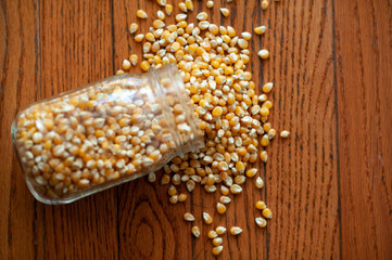 Popcorn kernels spilling out of mason jar onto wood surface