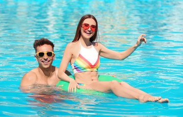 Happy young couple with inflatable ring in swimming pool