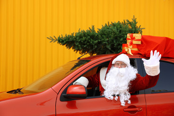 Obraz premium Authentic Santa Claus with fir tree and bag full of presents driving car against yellow background