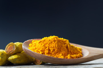 Turmeric peeled root and turmeric powder in wooden spoon or shovel on wooden rustic background, healthy spice curcumin ( curcuma longa )