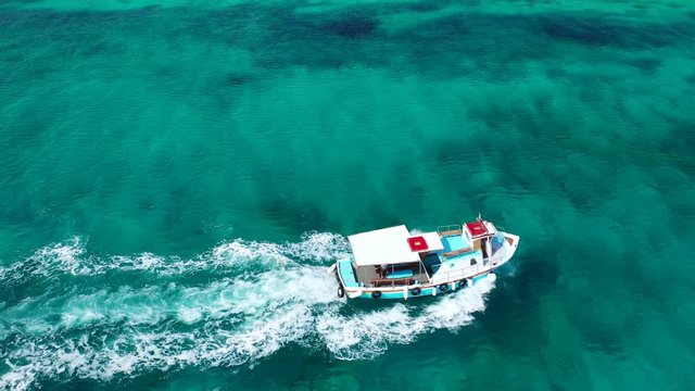 Aerial bird's eye view video taken by drone of boat cruising in Caribbean tropical beach with turquoise - sapphire waters