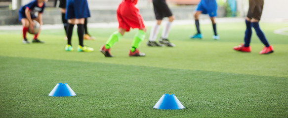 selective focus to blue marker cones are soccer training equipment on green artificial turf with blurry kid players training background. material for training class of football academy.