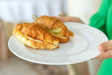 Hands holding a plate of croissant sandwiches