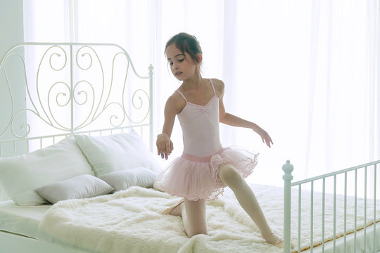 Cute pink dresses little girl 9 year dancing ballet with white bed in bedroom at home, Ballerina young girl practicing ballet dance at room. Kid ballet and performance art for modern concept.