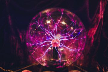 Hand touching a plasma ball with smooth magenta-blue flames.