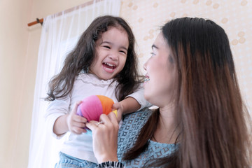 Joyful cute little girl holding small color ball toy in her hand while playing with mother in the bedroom. Smile cheerful daughter play ball with mom at their home. Lifestyle family concept.