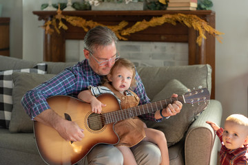 Grandfather with two young grandkids playing guitar on the couch