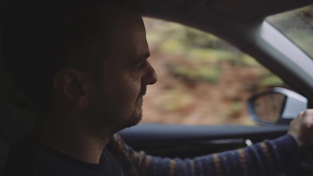 Man Driving a Car. SLOW MOTION. Portrait of a young handsome male driver navigating through fall countryside and forest on a rainy day.
