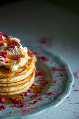 Stack of hotcakes with cream, dried raspberries and syrup