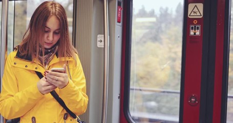 Young Woman Using Smartphone on a Train. SLOW MOTION 4K. Girl using cell phone standing by the train door during her daily commute. Social network, planning, communicating.