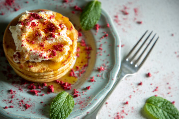 Stack of hotcakes with cream, dried raspberries and syrup