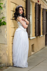 Obraz premium Portrait of Caucasian Brunette Bride with Tiara Posing Against Old Building. Wearing Beads Necklace and Decorations.