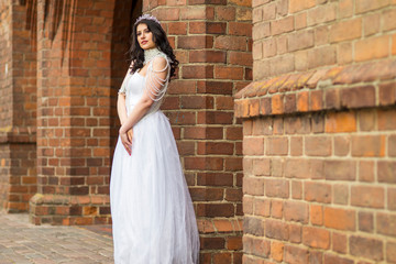 Fototapeta premium Portrait of Romantic Sensual Caucasian Bride With Crown And Necklace Posing Against Old Brick Wall Outdoos.