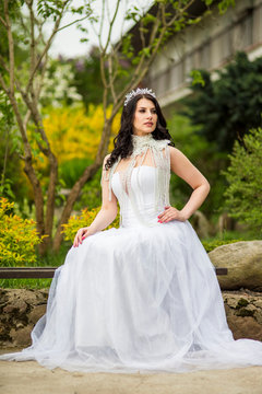 Portrait of Caucasian Bride With Diadem Sitting In Flowers Garden Outdoors. Wearing Beads Necklace.