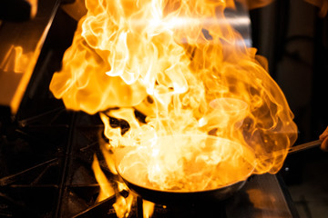 A chef man cook cooking a flame meal with a pan, fire and flame, flambing food
