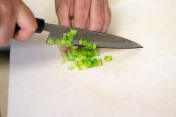 Closeup on a cook man chopping fresh celery with a kitchen knife in his Vancouver restaurant kitchen