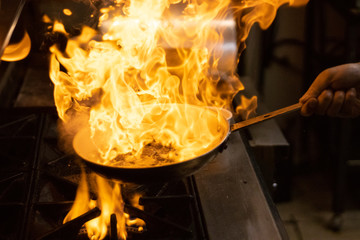 A chef man cook cooking a flame mushrooms with a fire pan, frying food
