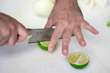 Closeup on a Chef man cutting a fresh green lime into four in his restaurant kitchen with a knife kitchen on a countertop