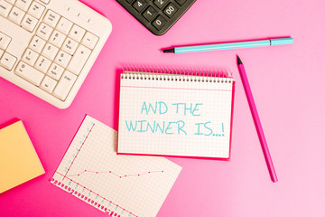 Word writing text And The Winner Is. Business photo showcasing announcing who got first place at competition or exam Writing equipments and computer stuffs placed above classic wooden table