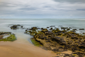 Rocks covered with marine foam. Long exposure on the coast. Silk effect in sea water.