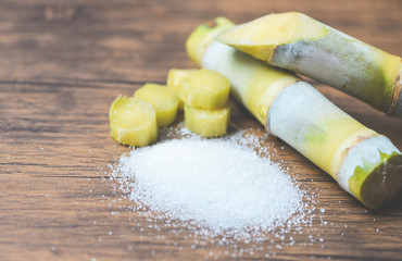 Cut sugar cane piece and white sugar on wooden background