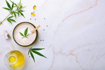Bank of medical cream with CBD oil, hemp leaf on a marble table. Flat lay, top view.