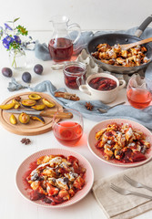 Kaiserschmarrn, Imperial pancake, traditional dessert of Austrian cuisine. White wooden table with pancakes, plum compote, fresh plums and pitcher with glasses of hibiscus tea.