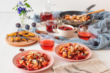 Kaiserschmarrn, Imperial pancake, traditional dessert of Austrian cuisine. White wooden table with pancakes, plum compote, fresh plums and pitcher with glasses of hibiscus tea.