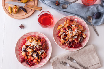 Kaiserschmarrn, Imperial pancake, traditional dessert of Austrian cuisine. White wooden table with pancakes, plum compote, fresh plums and pitcher with glasses of hibiscus tea.