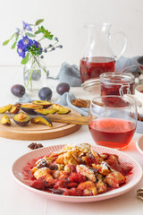 Kaiserschmarrn, Imperial pancake, traditional dessert of Austrian cuisine. White wooden table with pancakes, plum compote, fresh plums and pitcher with glasses of hibiscus tea.