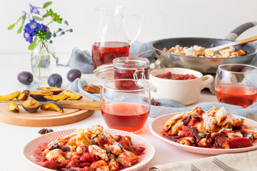Kaiserschmarrn, Imperial pancake, traditional dessert of Austrian cuisine. White wooden table with pancakes, plum compote, fresh plums and pitcher with glasses of hibiscus tea.