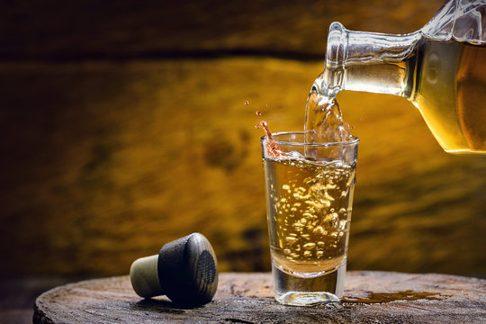 Glass of golden rum, with bottle. Bottle pouring alcohol into a small glass. Brazilian export type drink