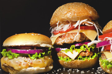 Fast food concept: fat burgers with cheese and vegetables on a dark background